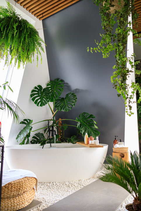 Luxe badkamer met vrijstaand bad, omringd door tropisch groen en meerdere kunst hangplanten voor een natuurlijke, spa-achtige sfeer.
